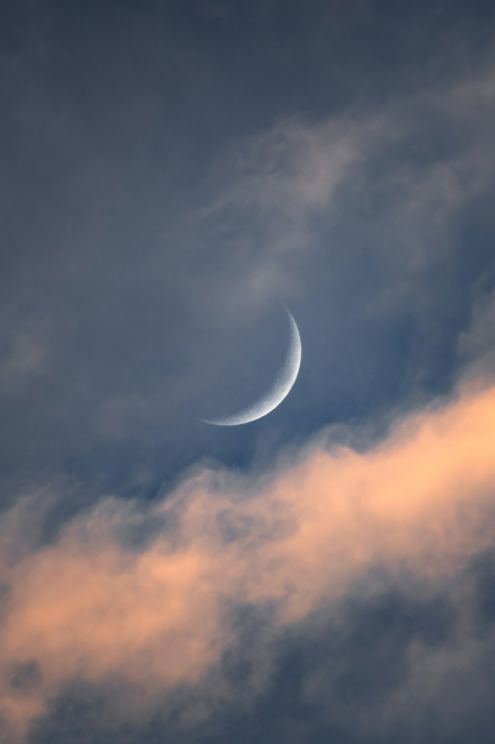 Eine Mondsichel ist durch einen bewölkten Himmel zu sehen