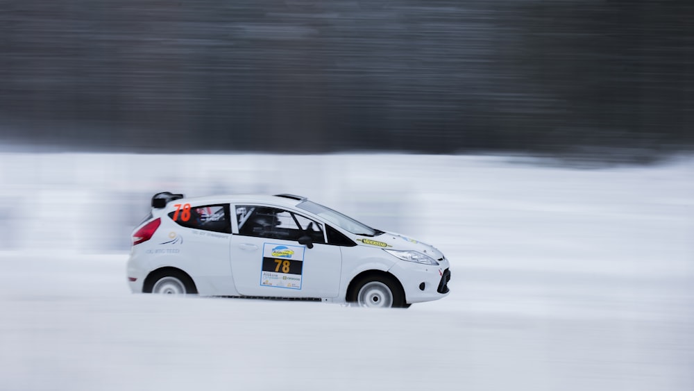 a small white car driving through a snow covered field