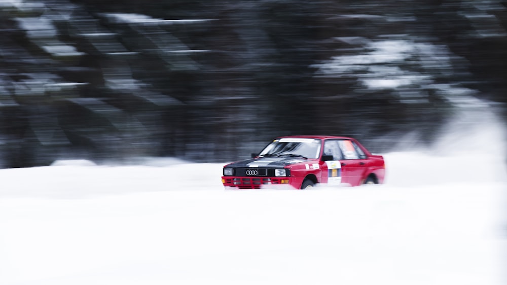 a red car driving down a snow covered road