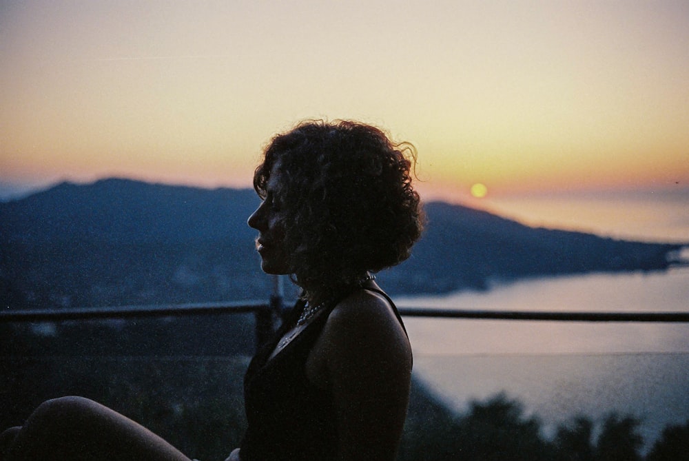 uma mulher sentada em cima de uma varanda ao lado de um pôr do sol