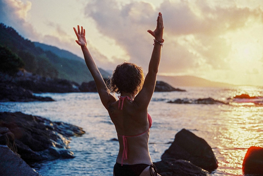 a woman in a bikini standing on a rocky beach