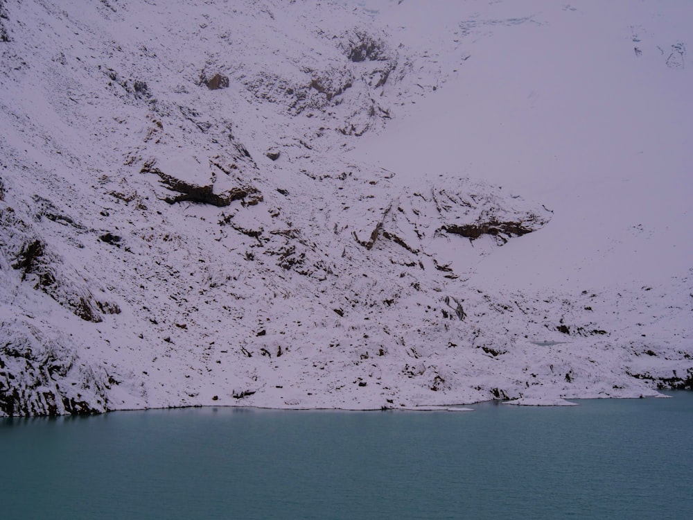 a mountain covered in snow next to a body of water