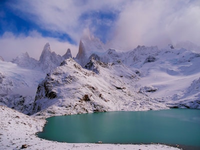 a snow covered mountain range with a lake in the foreground