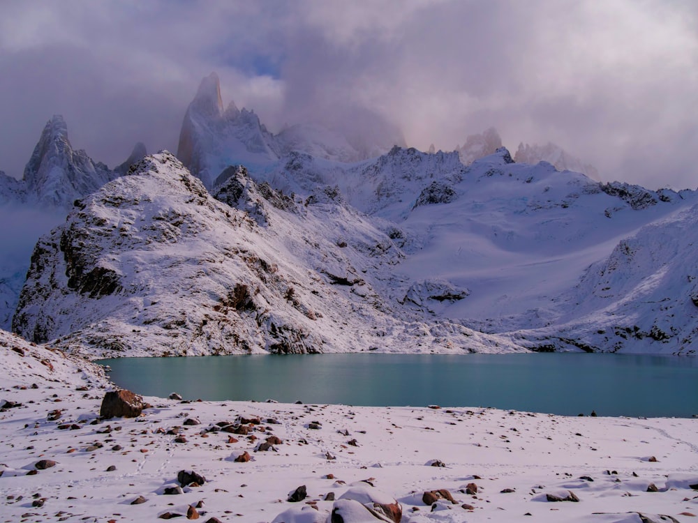 a snow covered mountain range with a lake in the foreground