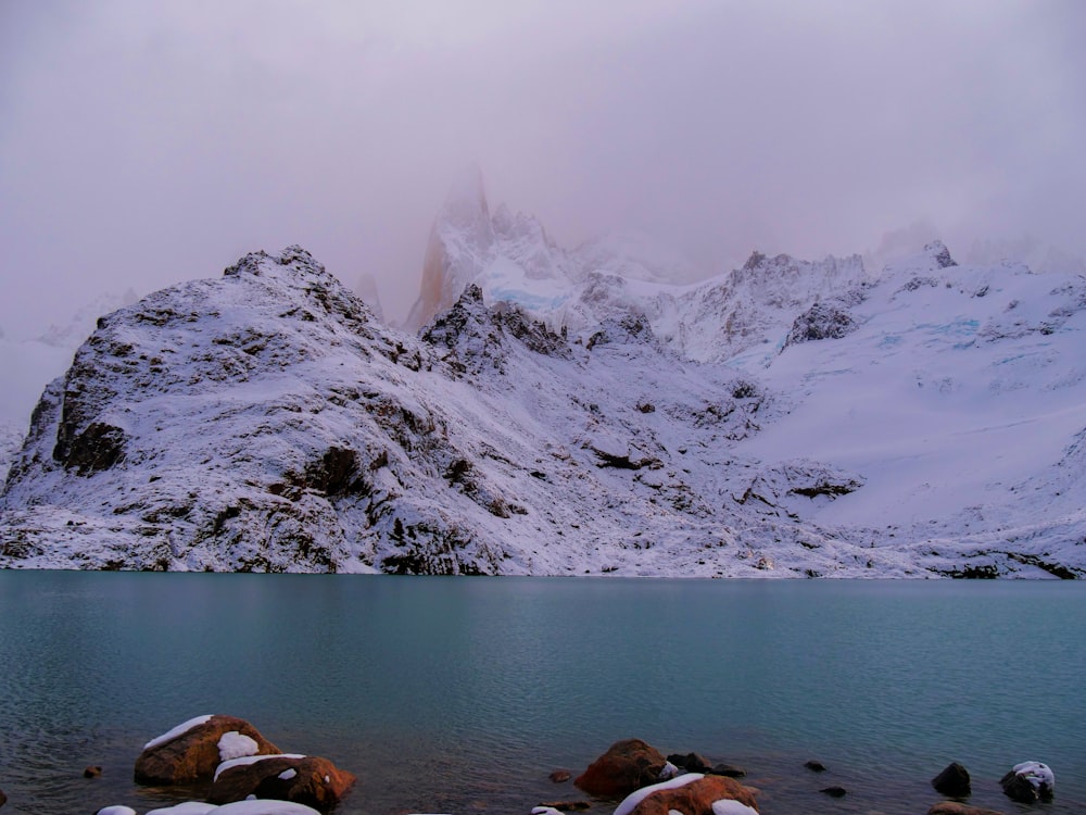 a mountain covered in snow next to a body of water