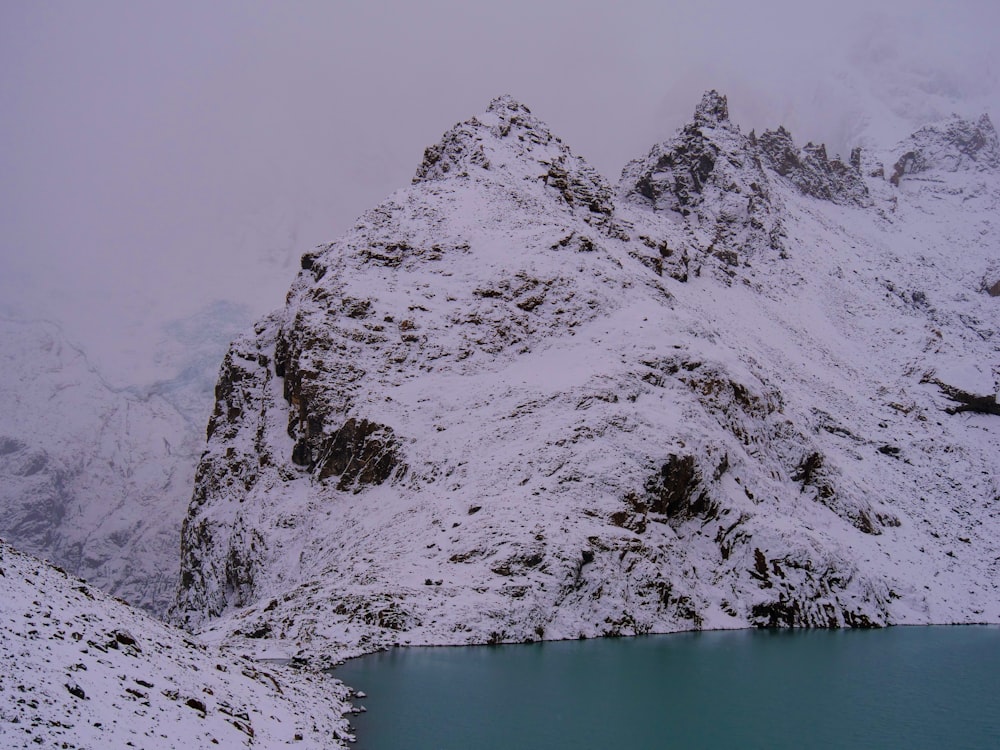 a mountain covered in snow next to a lake