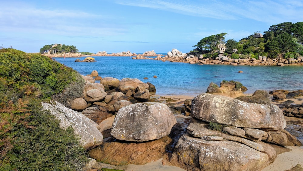 a rocky beach with large rocks and a body of water in the background