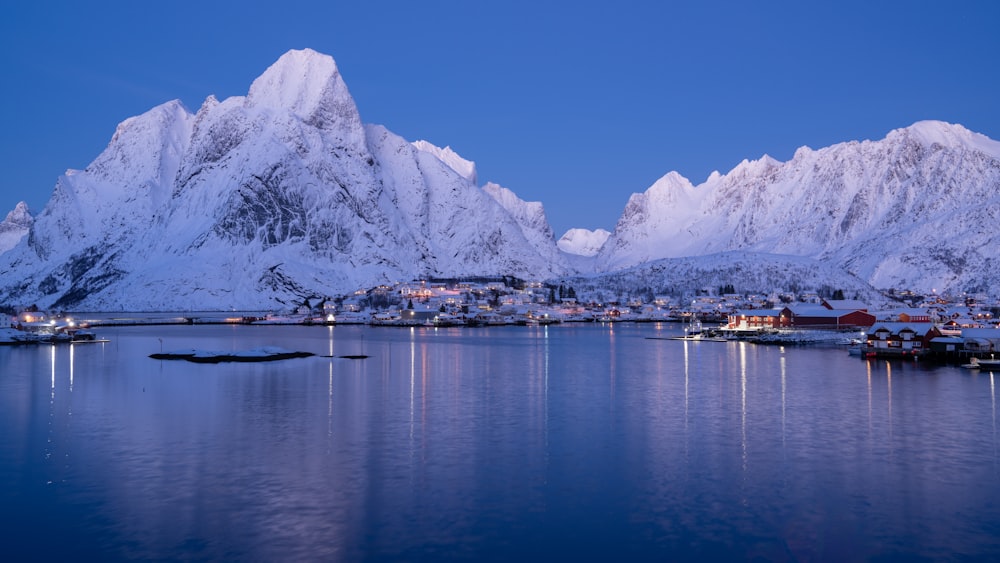 snow covered mountains rise above a small town on a lake