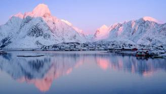 a snowy mountain range is reflected in the still water of a lake