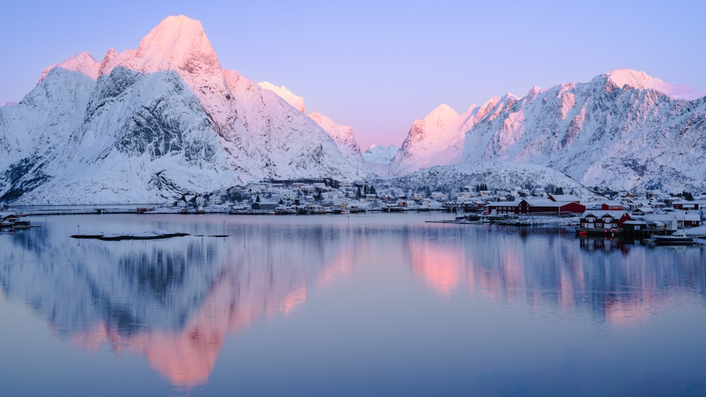 a snowy mountain range is reflected in the still water of a lake