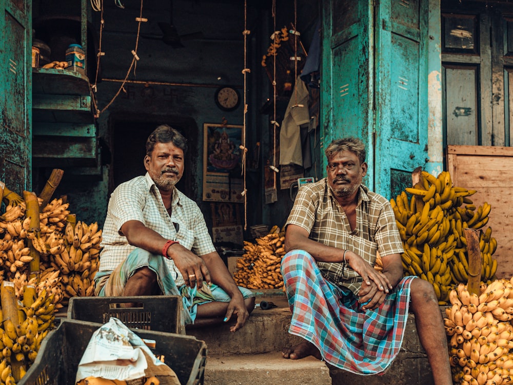 two men sitting in front of a bunch of bananas