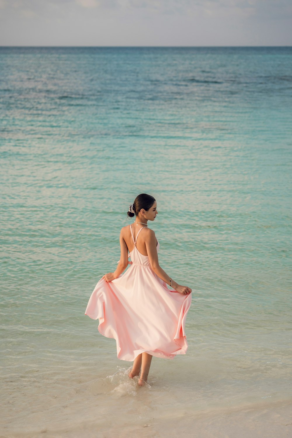 a woman in a pink dress walking into the ocean