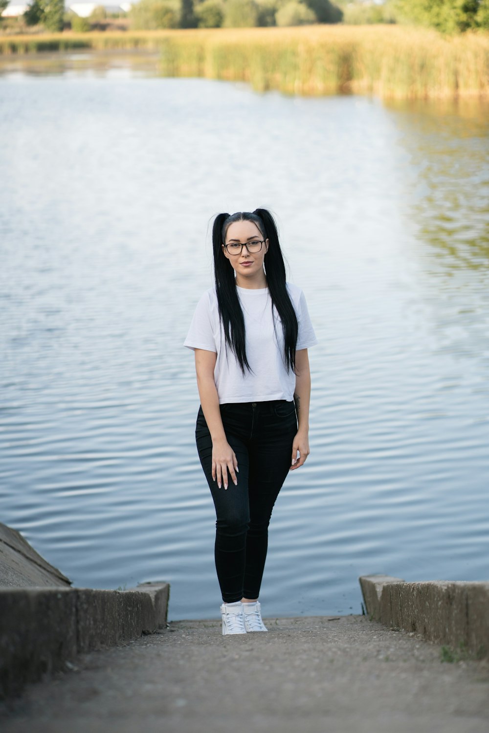 a woman with long black hair and glasses standing on steps near a body of water