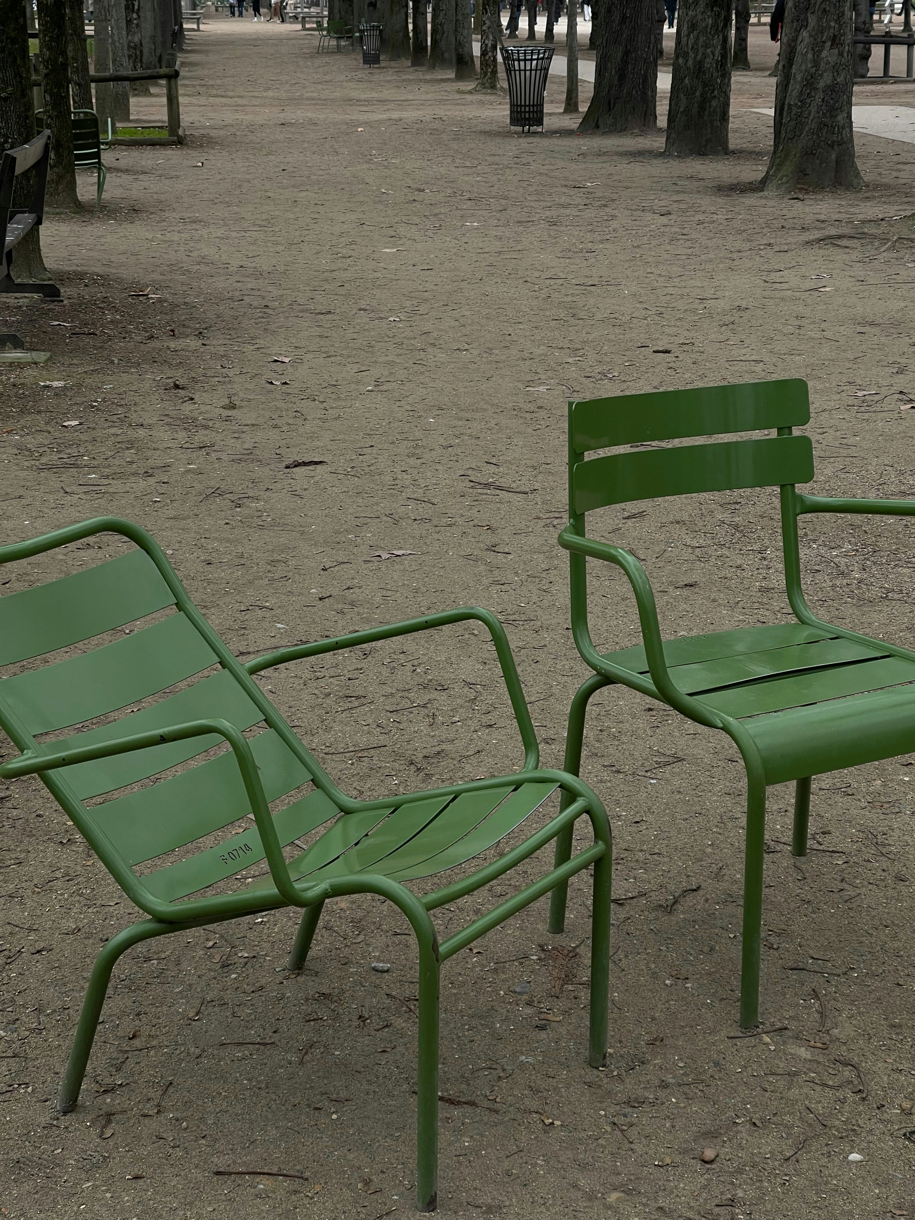 a couple of green chairs sitting on top of a dirt field