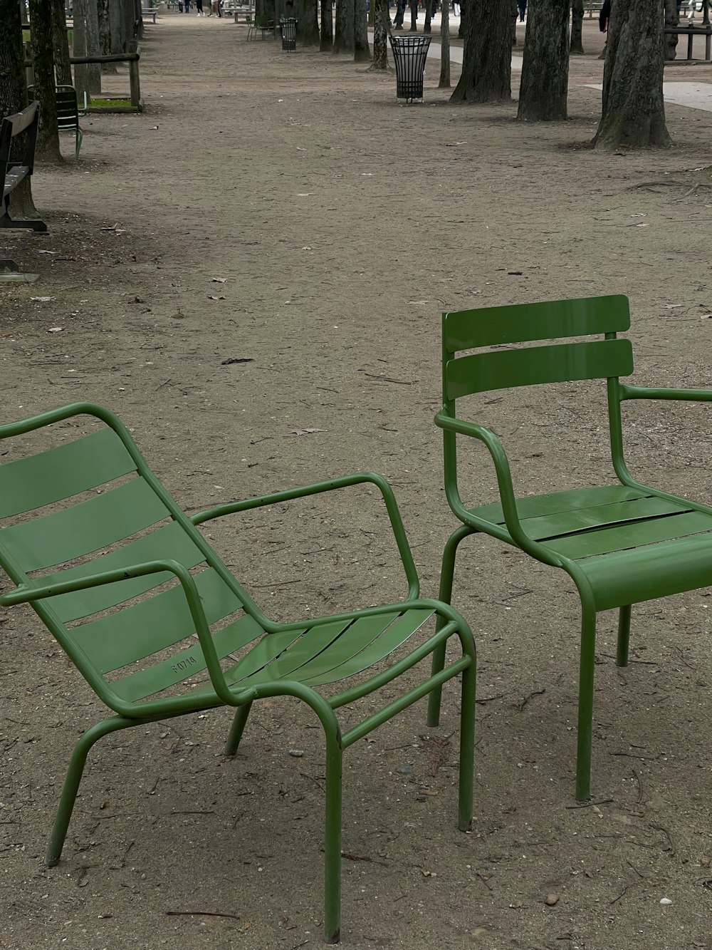 a couple of green chairs sitting on top of a dirt field