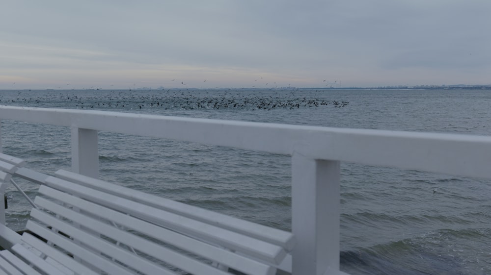 a white bench sitting on top of a pier next to the ocean