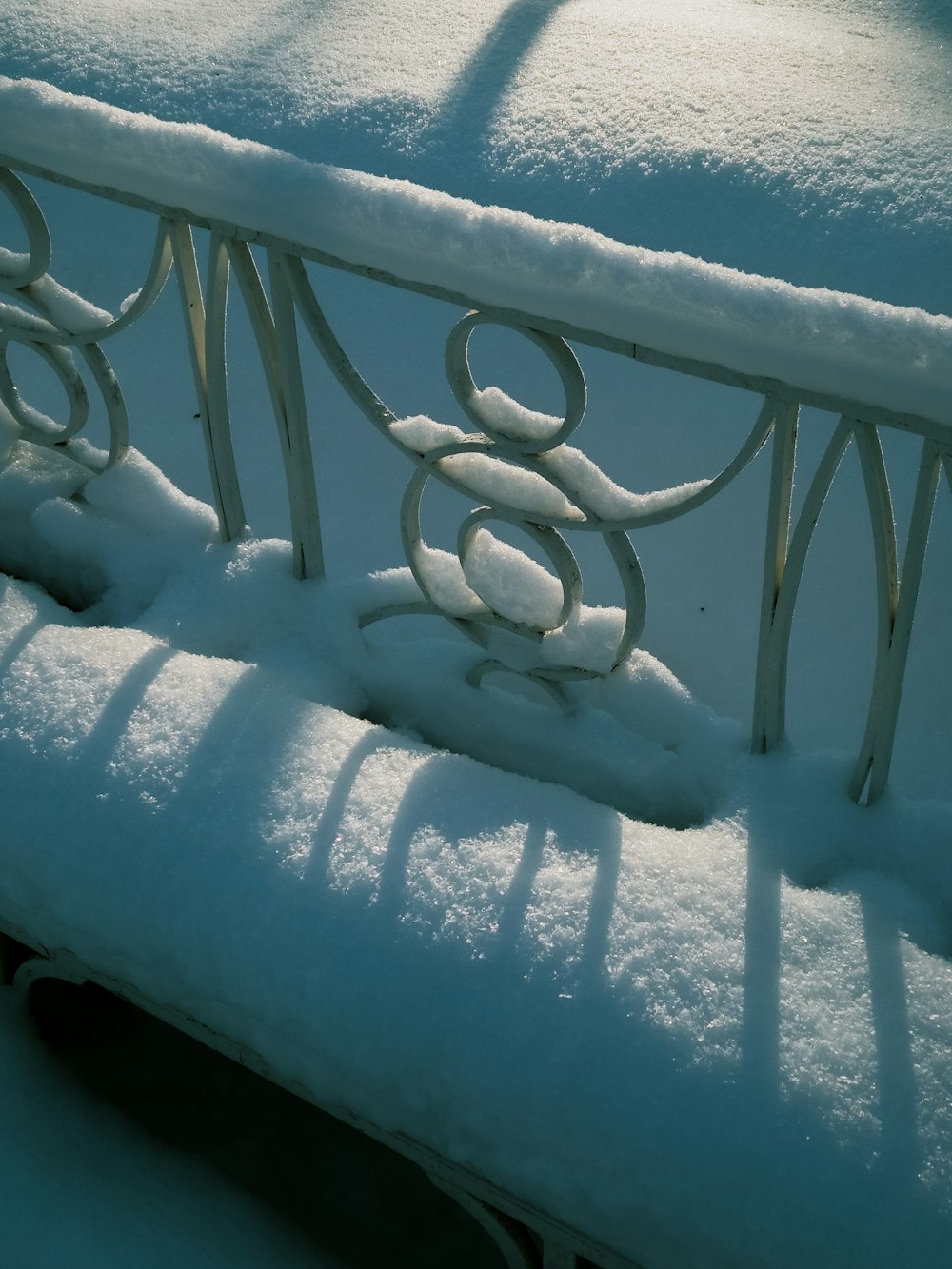 a bench covered in snow on a sunny day