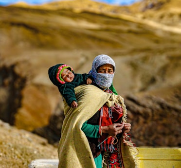 A Himachali lady dressed in vibrant traditional clothing, carrying her baby in the picturesque hills