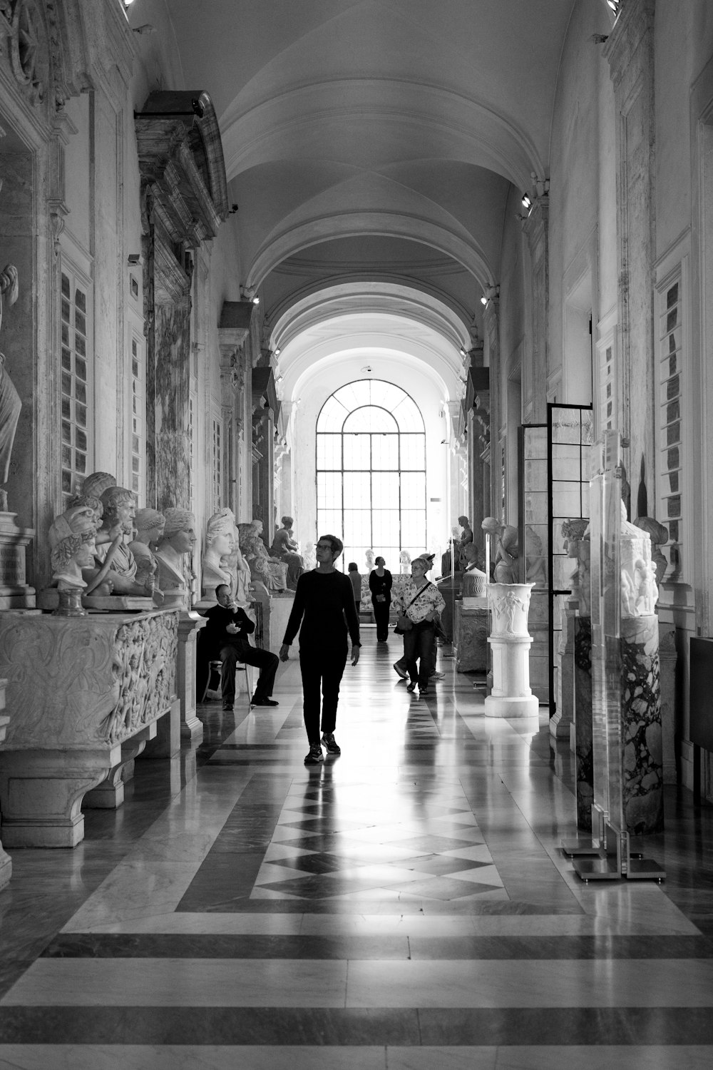 a black and white photo of a man walking down a hall