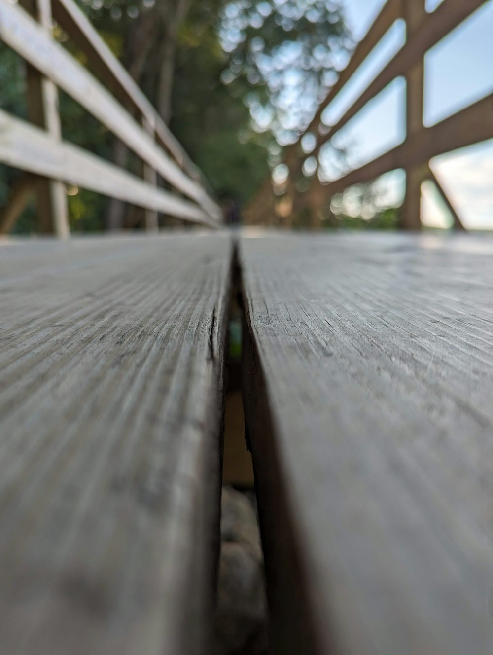 a close up of a wooden bench with trees in the background