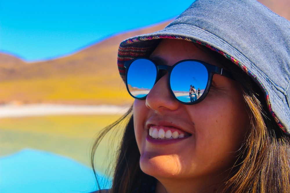 a woman wearing a hat and sunglasses with a lake in the background