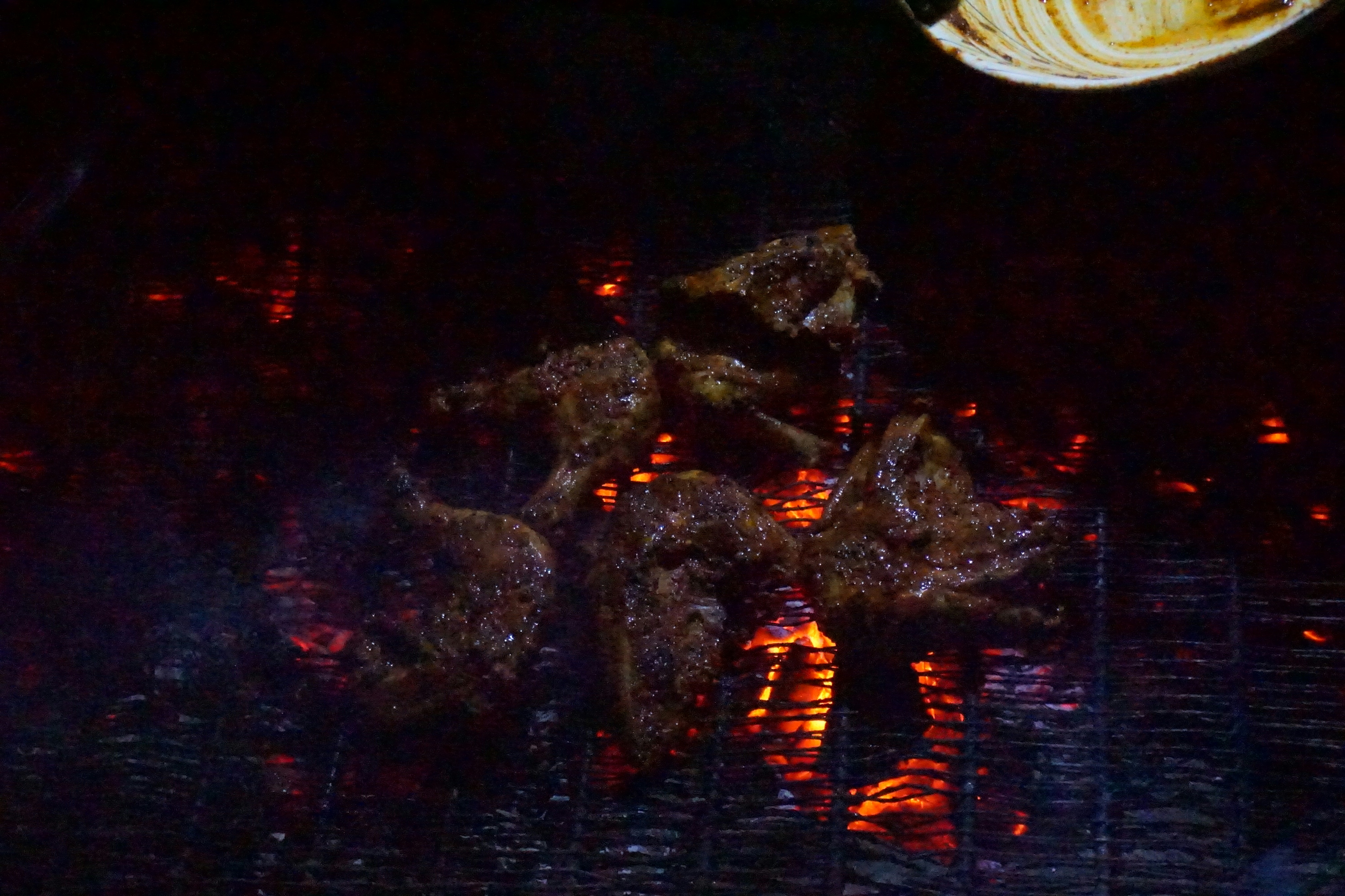 Grilled chicken with char marks on dark background, smoky embers visible, golden skin