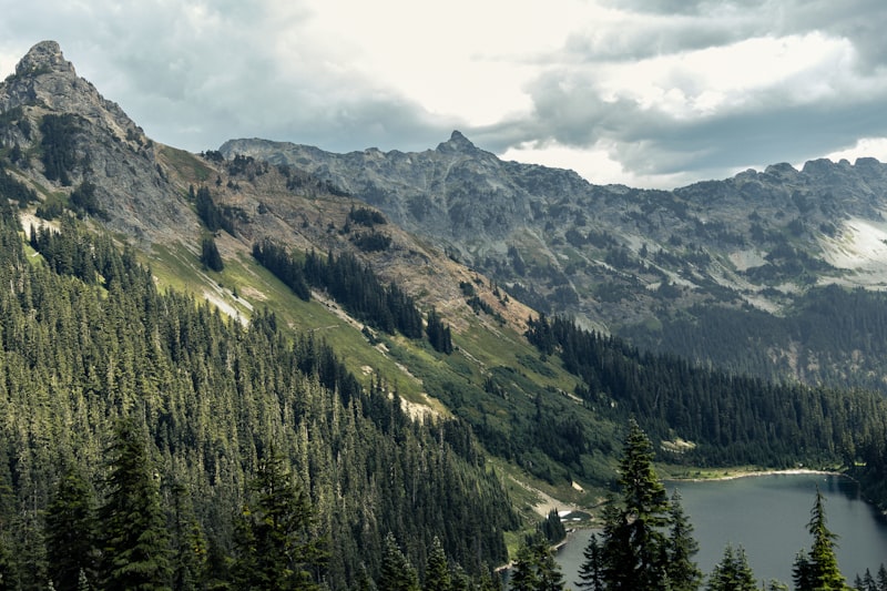 Jagged gray peaks above a forested valley and small alpine lake under scattered clouds in the Cascades