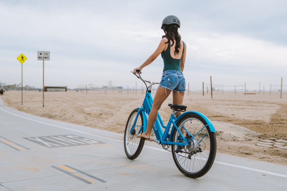 a woman riding a blue bike on a beach