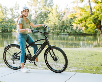 a woman riding a bike on a sidewalk next to a lake