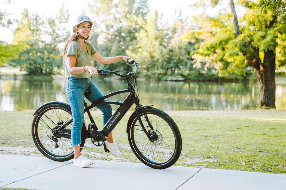 a woman riding a bike on a sidewalk next to a lake