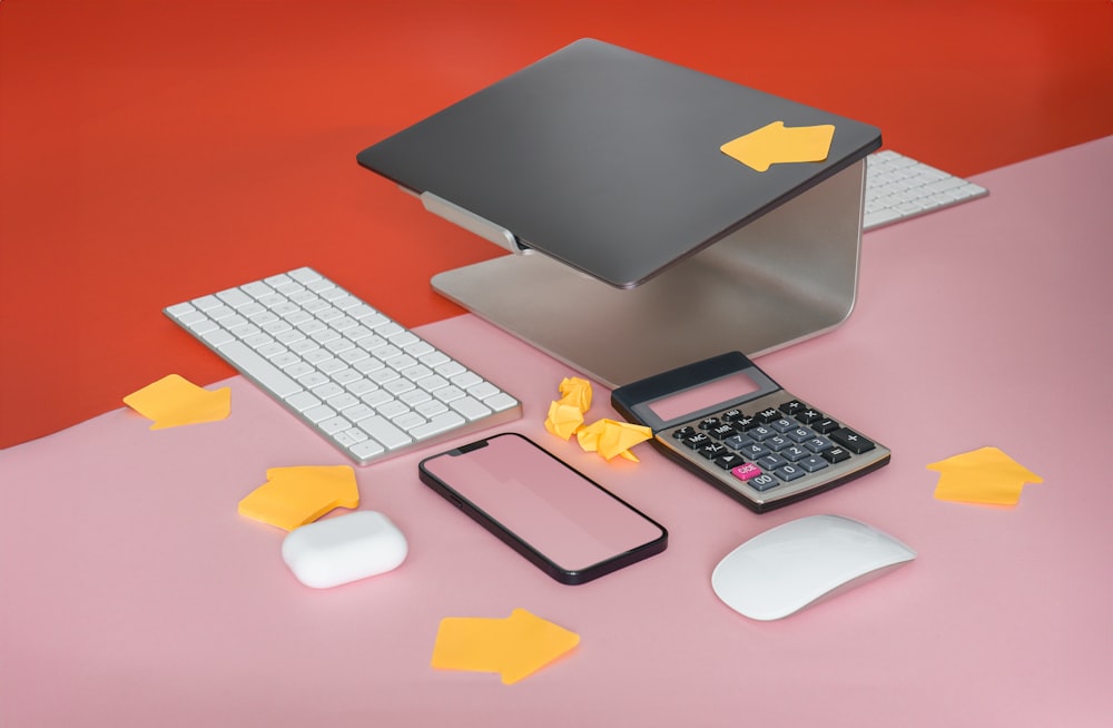 um telefone celular, teclado, mouse e mouse pad em uma superfície rosa