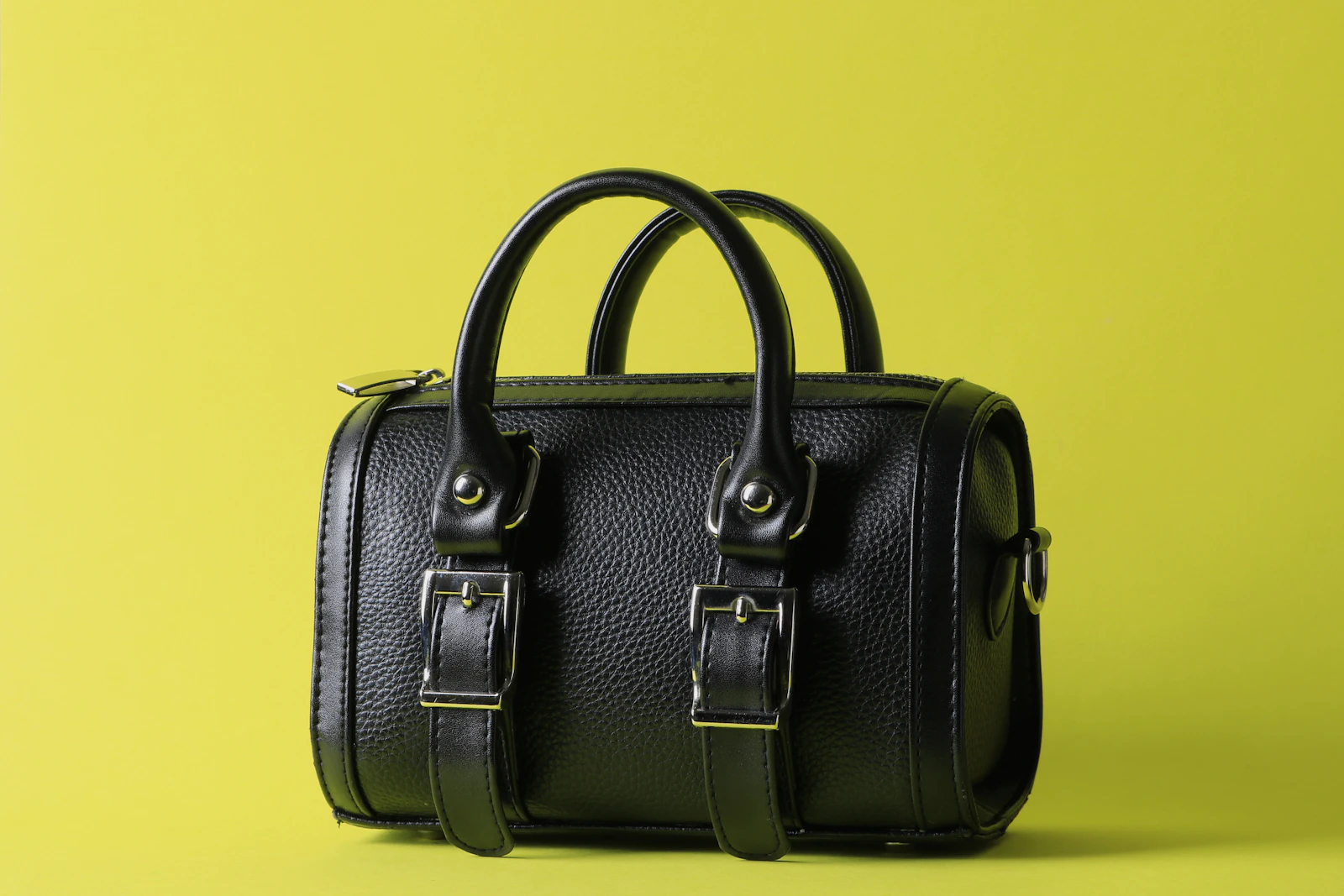 Sac à main en cuir noir à double anse posé sur un fond coloré