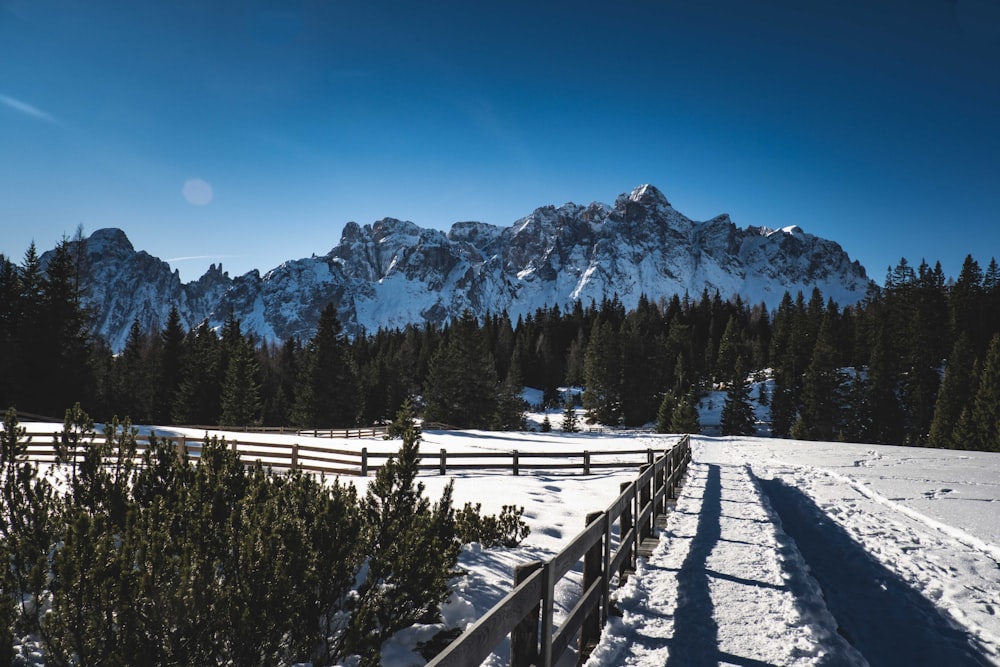 a snow covered field with a fence and mountains in the background