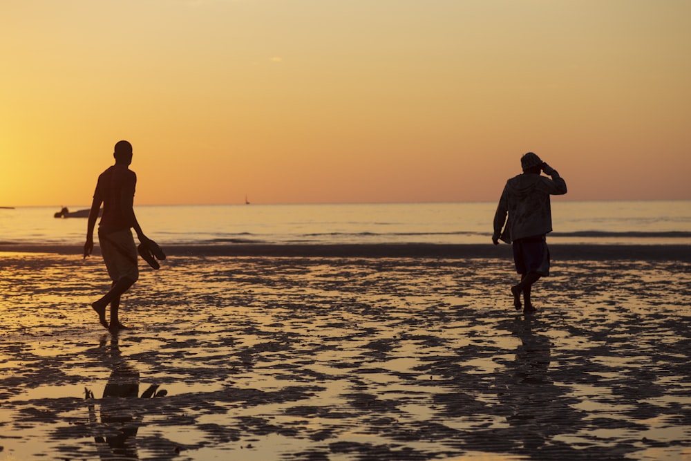 two people walking on a beach at sunset