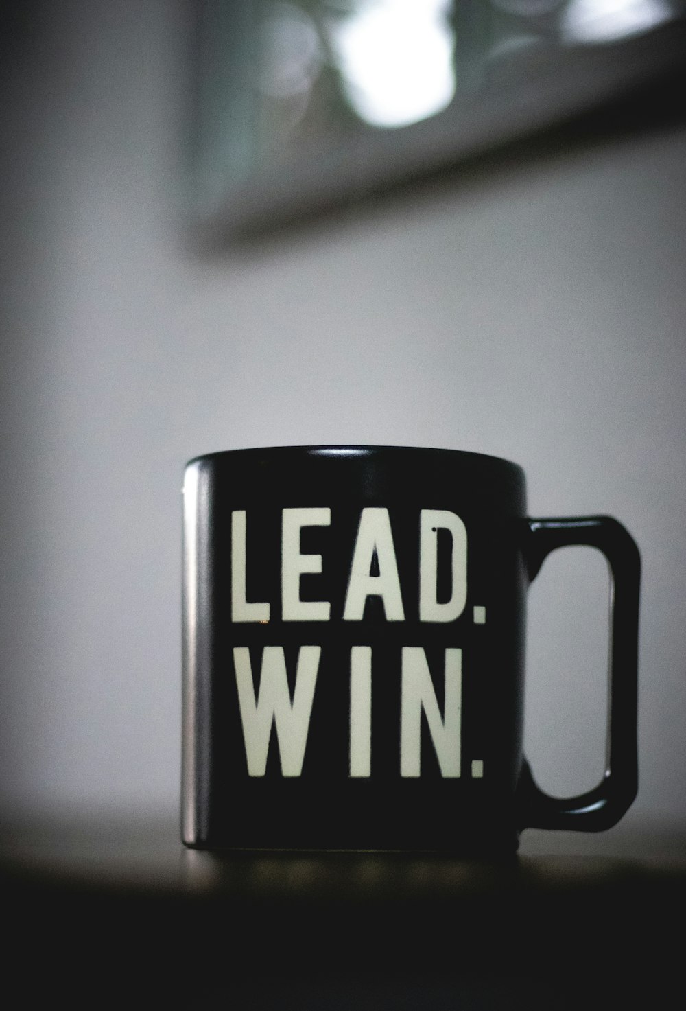 a black coffee mug with the words lead win printed on it