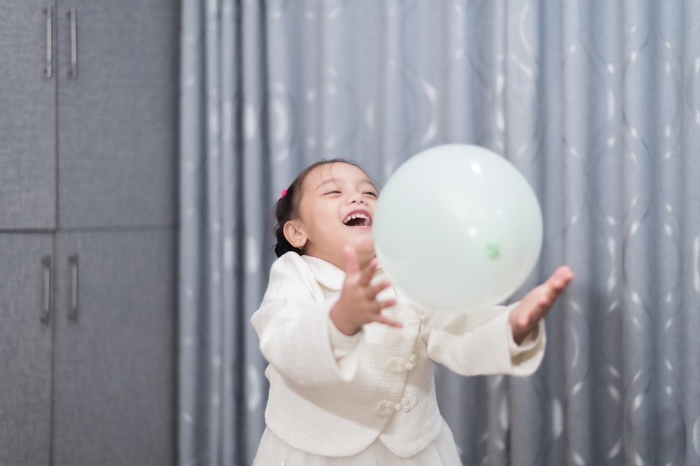 a little girl holding a white balloon in her hand