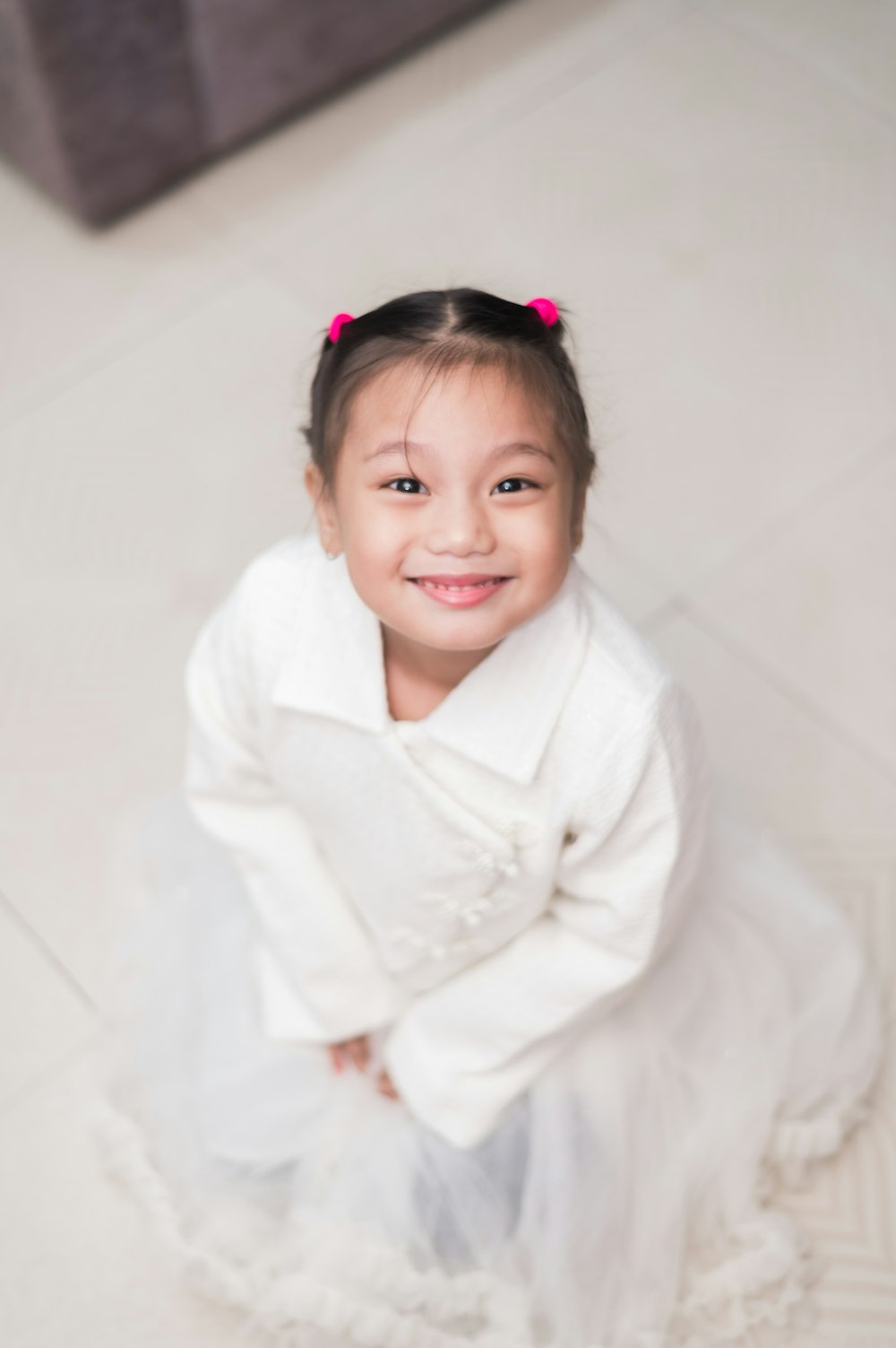 a little girl sitting on the floor in a white dress