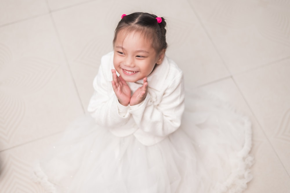 a little girl in a white dress sitting on the floor