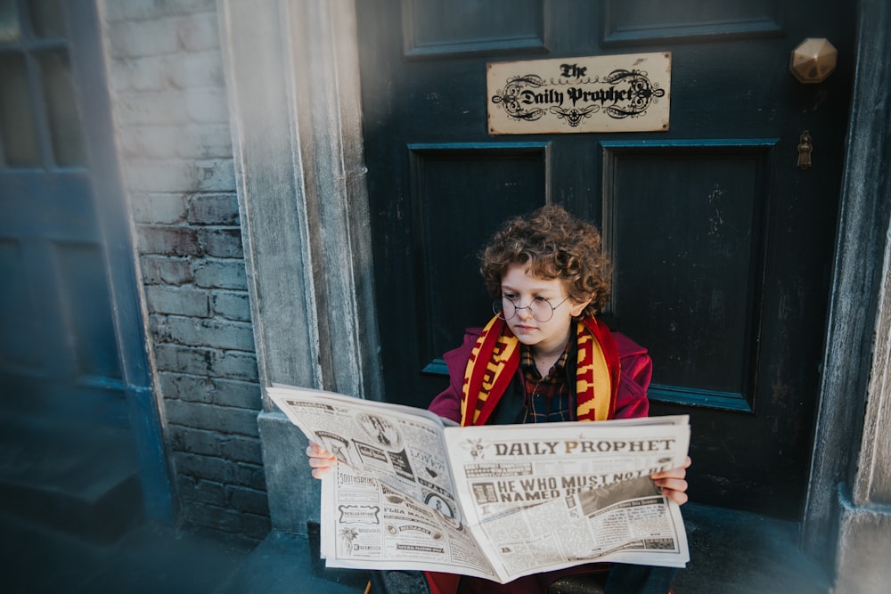 a young boy reading a newspaper in front of a door