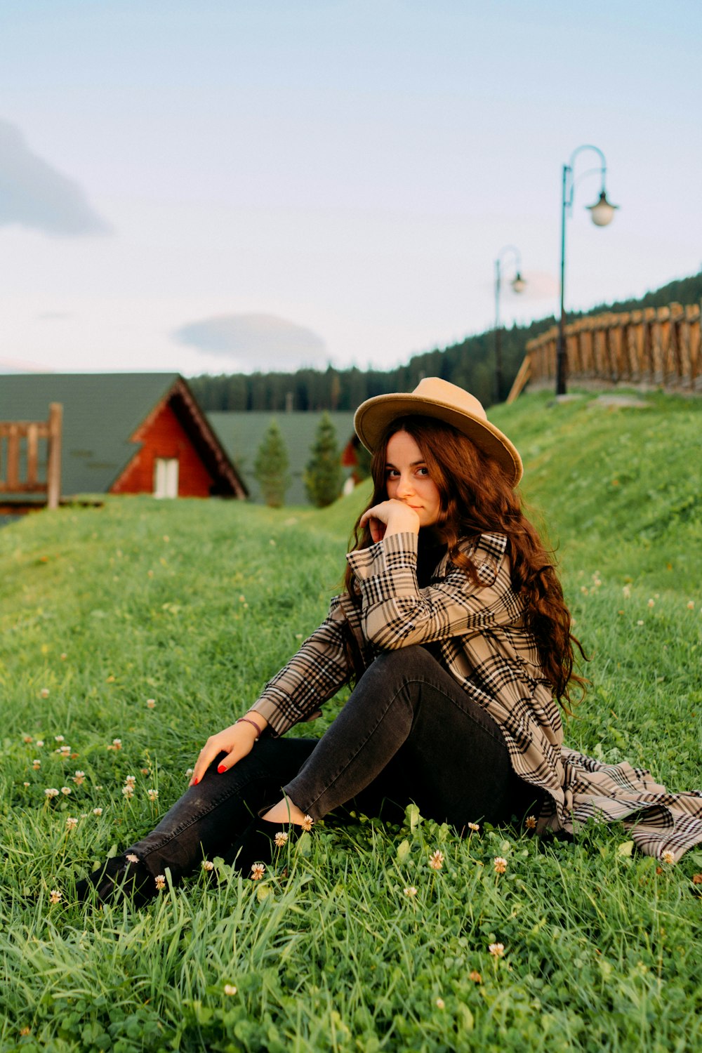 a woman sitting in the grass wearing a hat