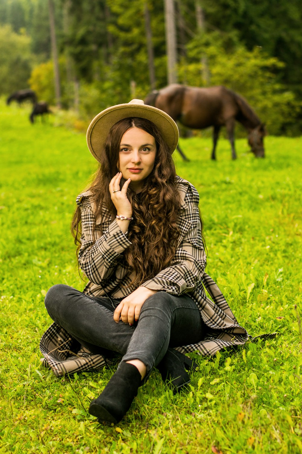 a woman sitting on the grass with a horse in the background