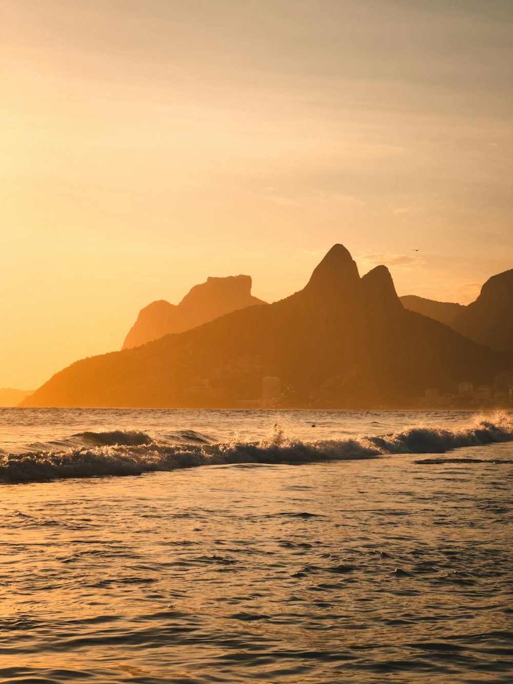 the sun is setting over the ocean with mountains in the background