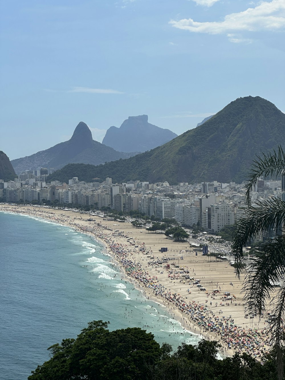 a crowded beach with mountains in the background