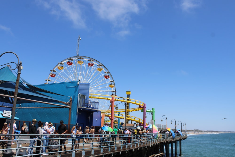 a crowd of people standing on a pier next to a ferris wheel