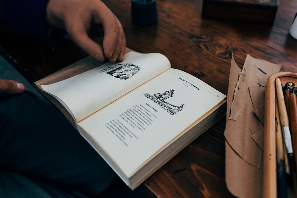 una persona sosteniendo un libro abierto encima de una mesa de madera