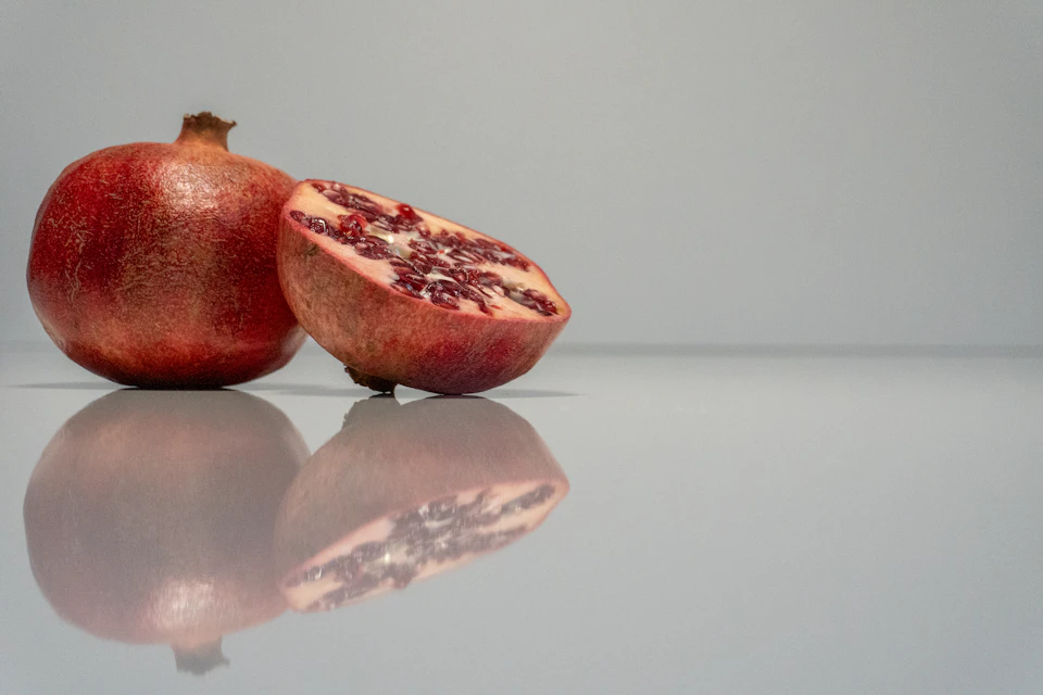 Two pomegranates, one whole and one cut open, on a white surface against gray background