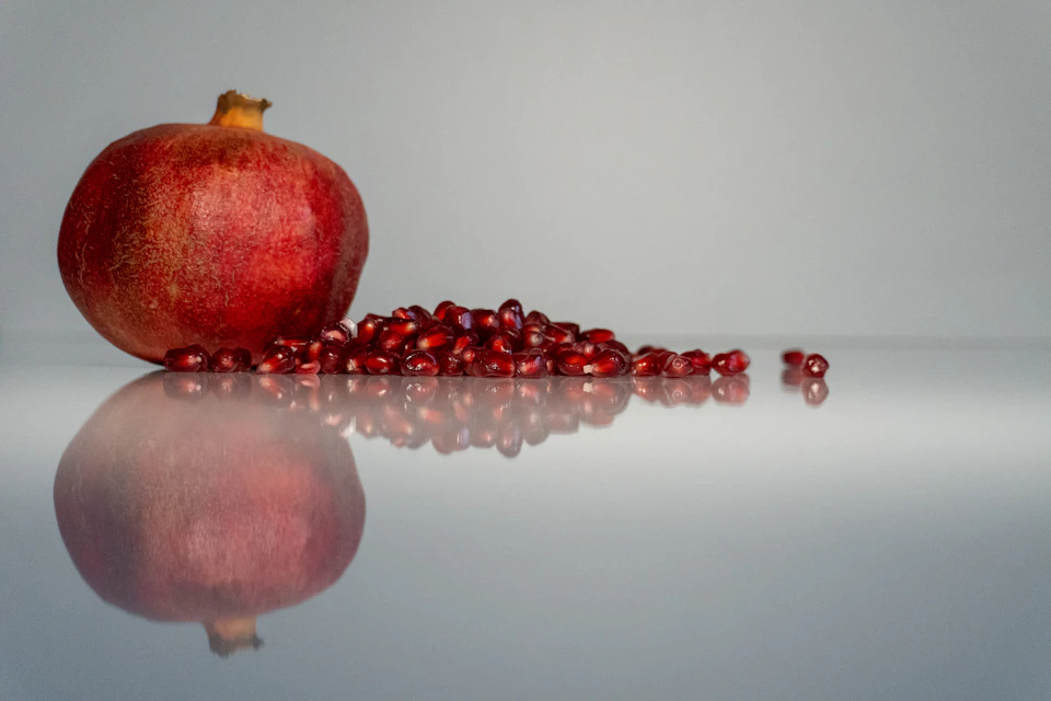 Vibrant red pomegranate on a white surface, surrounded by scattered seeds and contrasting red accents