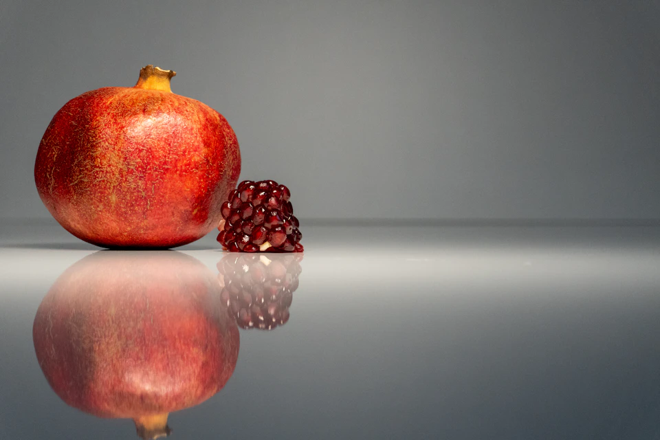 Close-up view of pomegranate and raspberry resting on gray surface with reflected images