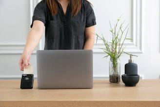 a woman standing at a desk with a laptop and a phone
