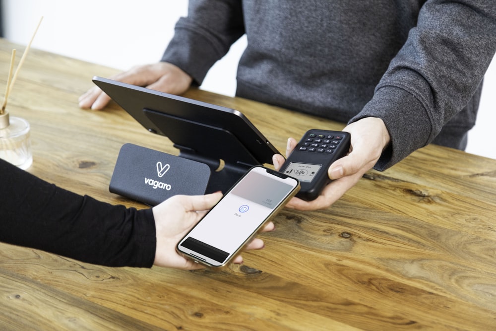 a person holding a cell phone and a laptop on a table